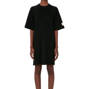 Modeled front view of a cotton Open Back T-shirt Dress, pictured against a white background from neck to ankle. The dress features a logo on the sleeve and hits just above the knee.