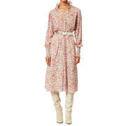 Model wearing a printed cotton dress with long sleeves. The dress has a ruffled high neck with buttons and a pink and orange pattern. It is cinched at the waist and styled with a white belt and knee-high boots. The sleeves are ruched with ruffles. The model is shown against a white background, from chin to foot.
