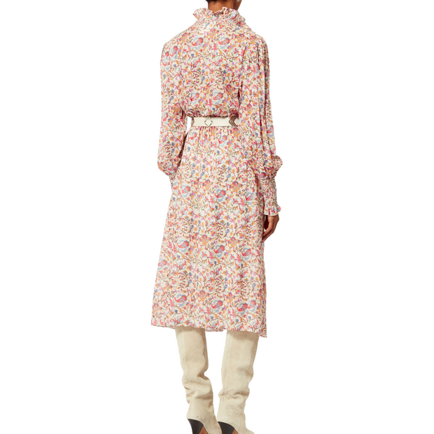 Back view of a model wearing a printed cotton dress with long sleeves. The dress has a ruffled high neck with buttons and a pink and orange pattern. It is cinched at the waist and styled with a white belt and knee-high boots. The sleeves are ruched with ruffles. The model is shown against a white background, from chin to foot.